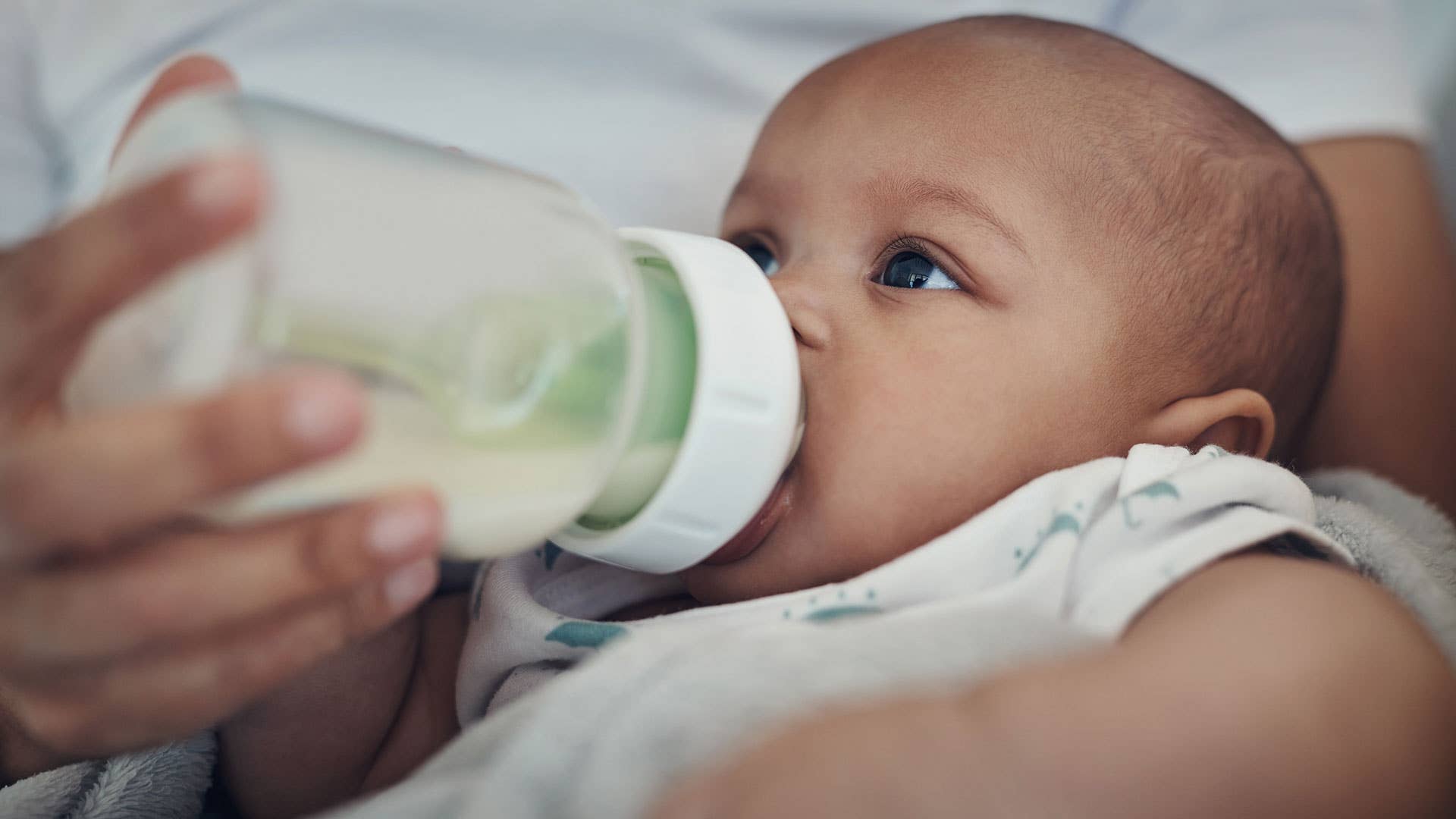 A baby drinks formula from a bottle. Baby Formula Lead JS