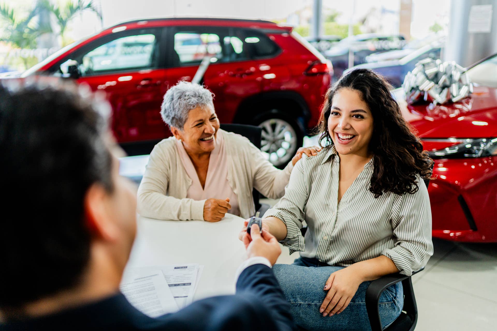 Mother and daughter receiving car key at car dealership