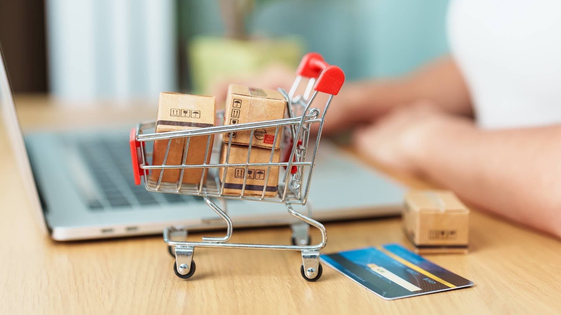 A person on laptop with mini shopping cart indicating e-commerce online shopping