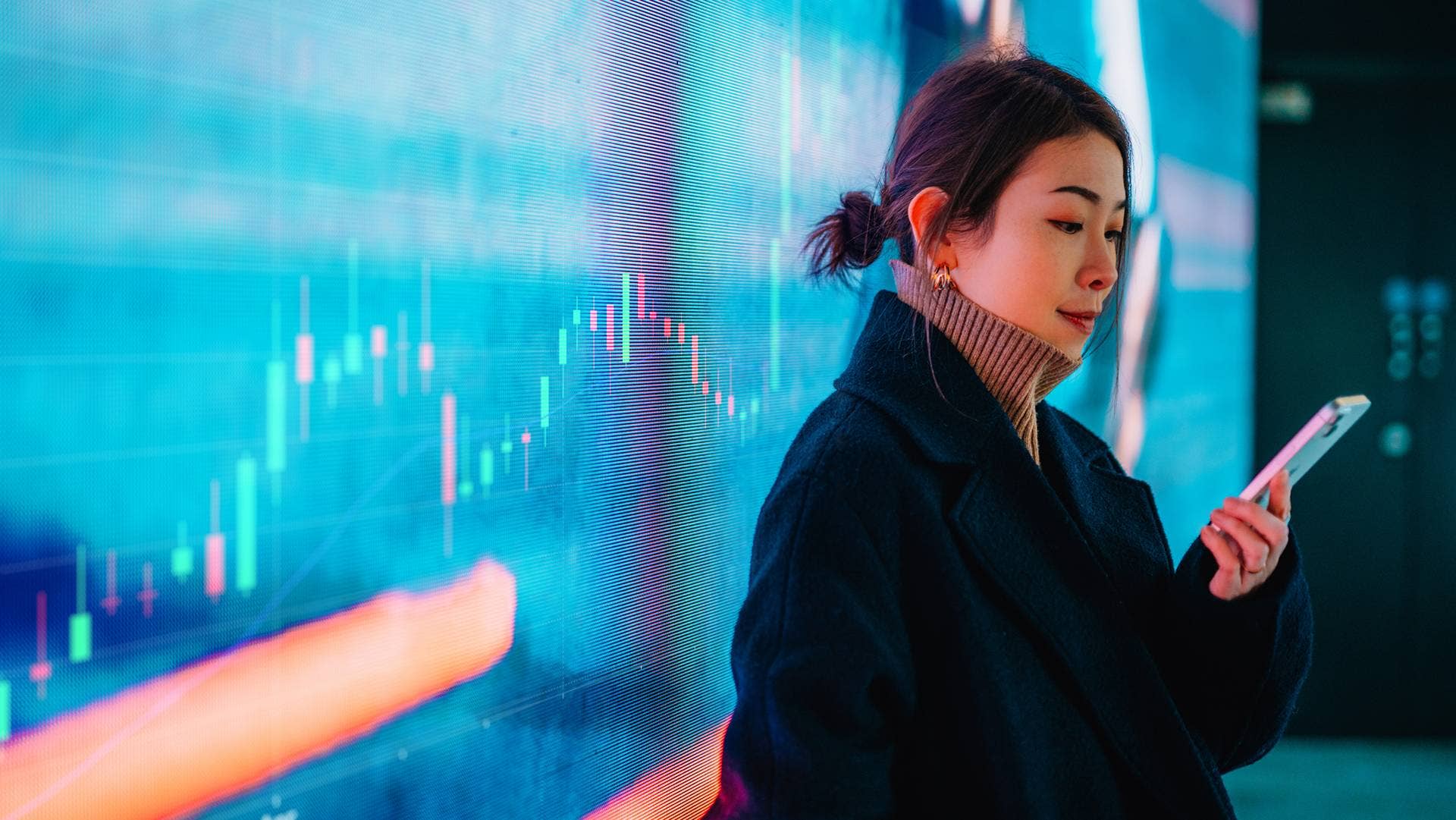 Businesswoman using a smartphone standing in front of a big screen