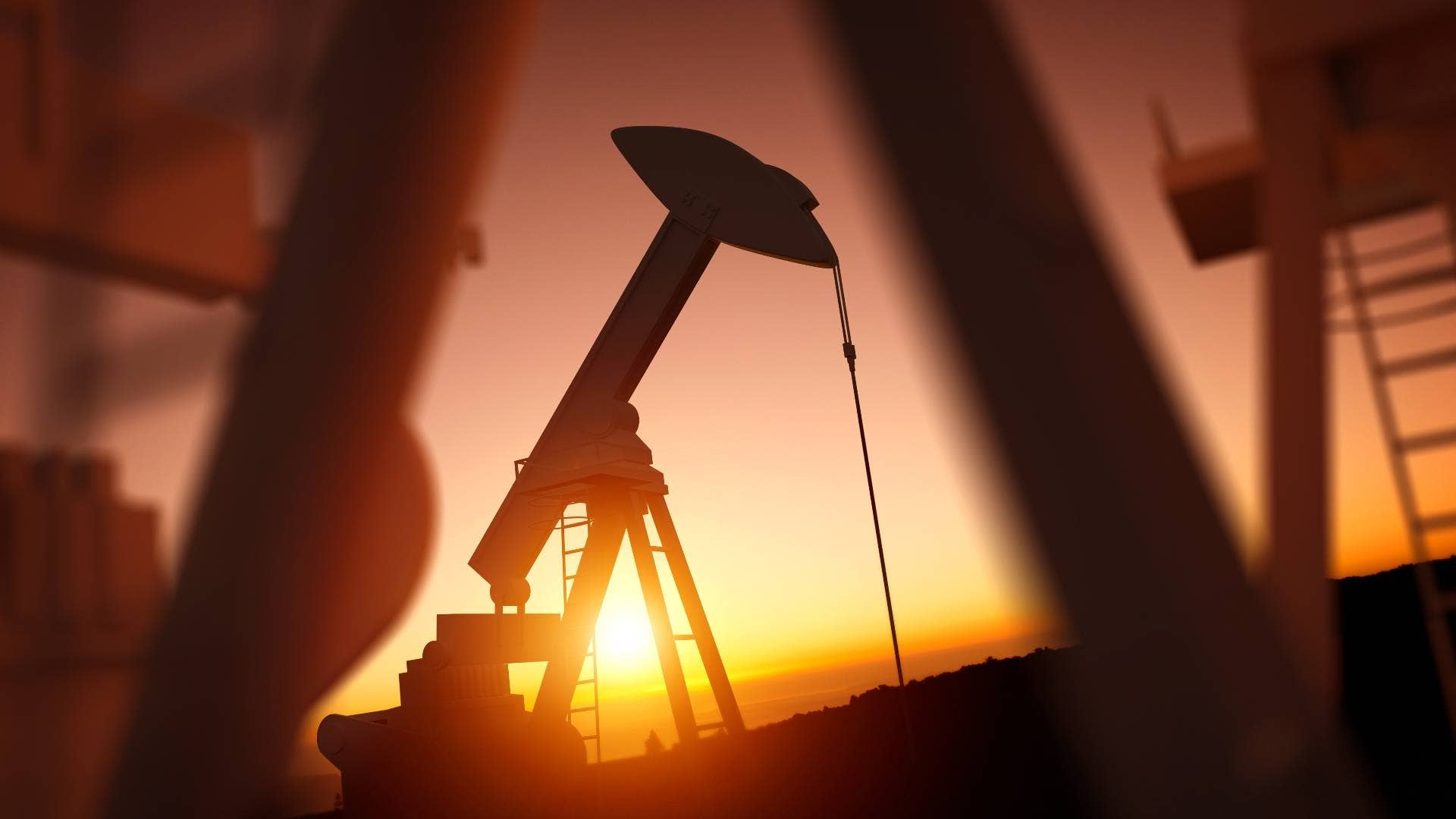 An oil rig is shown at sunset with the sun in the background.