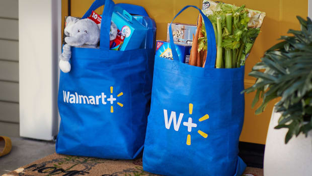 Two bags of Walmart groceries sit in front of a door. Walmart Plus Lead