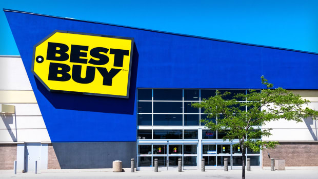The entrance of a Best Buy store location with a tree in front.