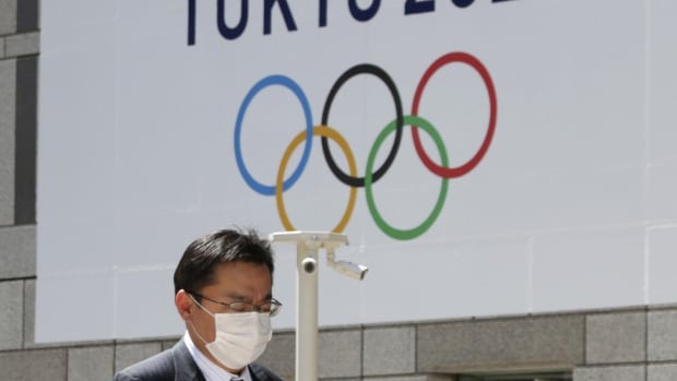 A masked man walks in front of a Tokyo Olympics logo at the Tokyo metropolitan government headquarters building in Tokyo on March 25, 2020. Photo: AP