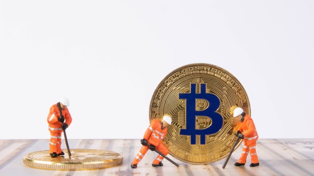 Toy figures hold mining equipment in front of physical bitcoin.