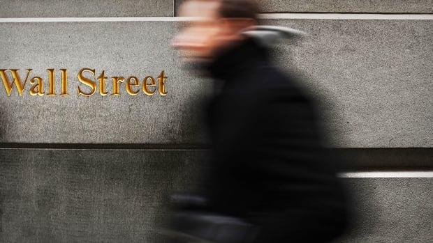 A man walks by a building with the words "Wall Street" in gold lettering on it.
