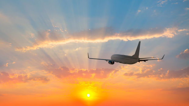 An unidentified airplane is seen flying over tropical sea at sunset. -lead