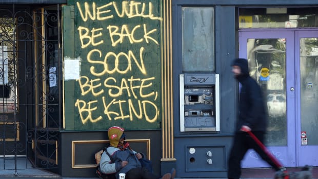 A man walks his dog past a homeless man sleeping under a message painted on a boarded up shop in San Francisco, California on April, 1, 2020, during the novel coronavirus outbreak. - The US death toll from the coronavirus pandemic topped 5,000 late on April 1, according to a running tally from Johns Hopkins University. (Photo by Josh Edelson / AFP) (Photo by JOSH EDELSON/AFP via Getty Images)