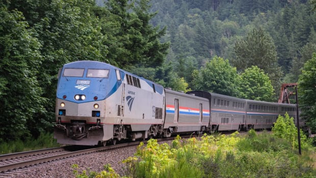 An Amtrak train is seen going through a green area. -lead