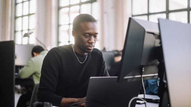 Focused male computer programmer working on laptop at desk in office