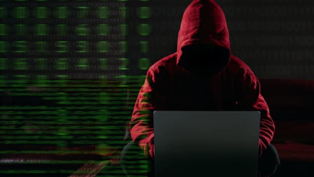 A hacking and malware concept: A hacker in a red hooded sweatshirt uses a laptop computer. Background is binary code.