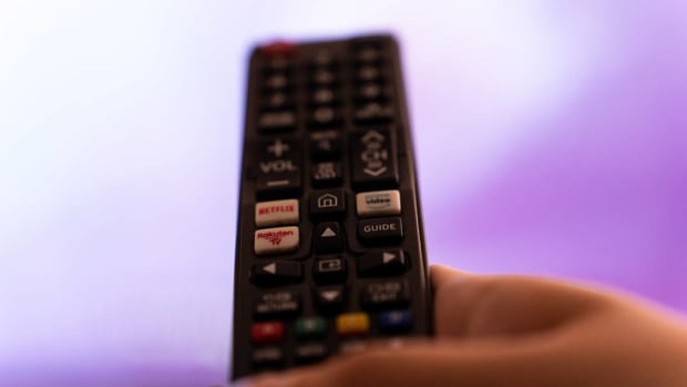 A hand holding a TV remote with shortcut buttons for Netflix, Amazon Prime Video, and Rakuten TV streaming platforms. lead.