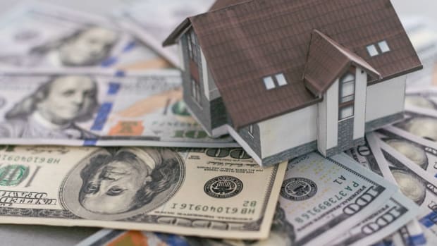 A small model home on a pile of money, showing the housing market for homebuyers. lead.