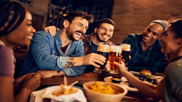 Group of young cheerful people toasting while drinking beer  in a pub. 