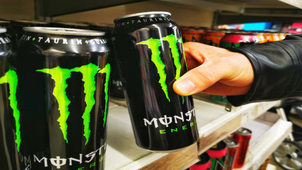 A young man takes a Monster Energy Drink can from a shelf. lead.