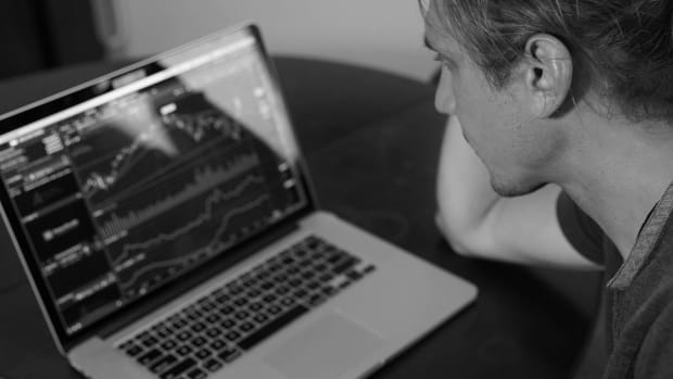 A person sits at a desk, closely looking at a laptop screen that displays multiple financial charts and stock market data. lead.