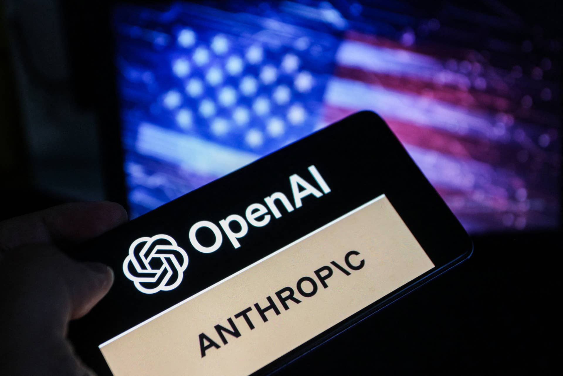 A smartphone screen displays the logos of OpenAI and Anthropic against a blurred backdrop of the American flag, symbolizing the intensifying competition in artificial intelligence between the two US-based companies in Tunis,Tunisia on June 17,2026.