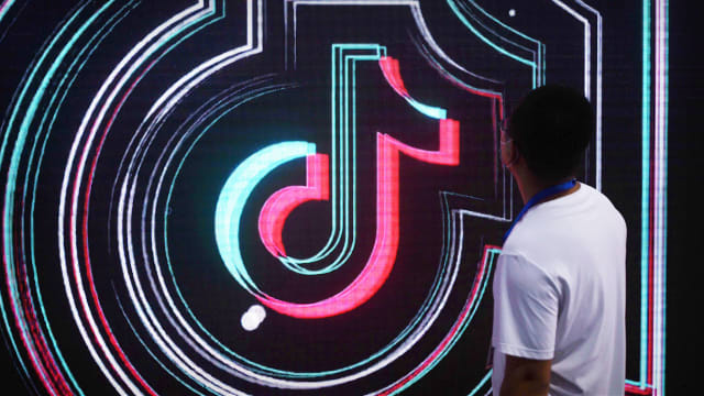 A person stands near a TikTok logo. Lead.