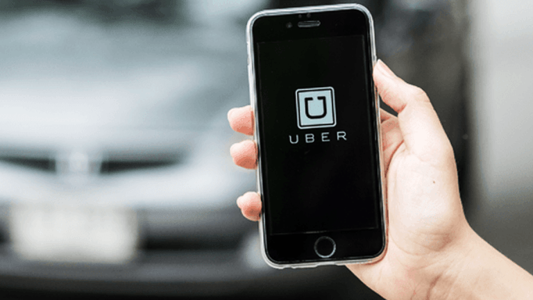 Una persona sostiene su smartphone mientras utiliza la aplicación Uber con un coche borroso de fondo