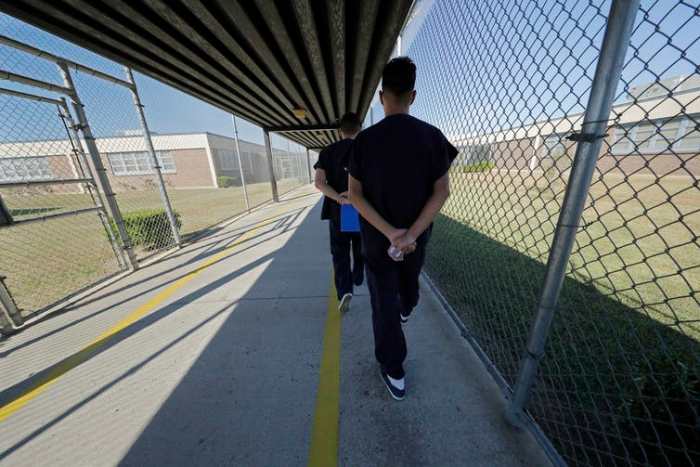 In this September 2019 photo, asylum-seekers walk with their hands clasped behind their backs along a line painted on a walkway inside a correctional centre Winnfield, La. (AP Photo/Gerald Herbert)