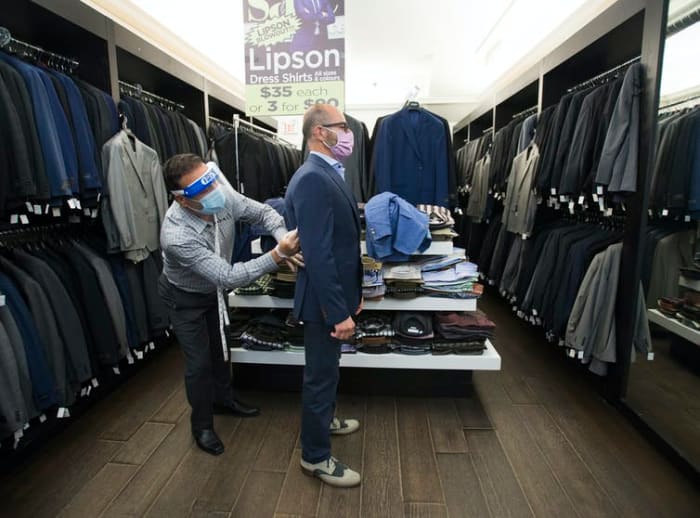 Head tailor Soheil Khorrami, left, demonstrates a safe way to fit a blazer for a customer at Tom’s Place in Kensington Market in Toronto in June 2020. THE CANADIAN PRESS/Nathan Denette