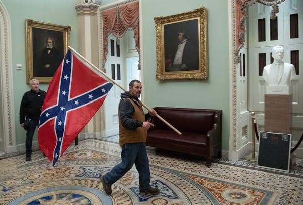 A man carries the Confederate battle flag in the U.S. Capitol on Jan. 6, between portraits of senators who both opposed and supported slavery. Saul Loeb/AFP via Getty Images
