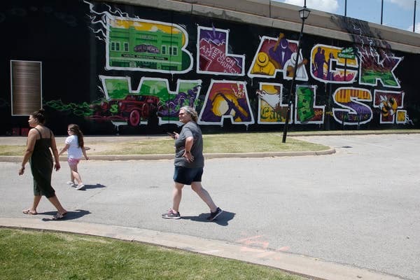 In this June 15, 2020, photo, people walk past a Black Wall Street mural in the Greenwood district in Tulsa, Okla. Dozens of blocks of Black-owned businesses were destroyed by a white mob in deadly race riots nearly a century ago. (AP Photo/Sue Ogrocki)