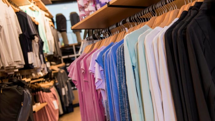 Assorted Lululemon Athletica activewear shirts and jackets hanging on racks inside a retail store. lead.