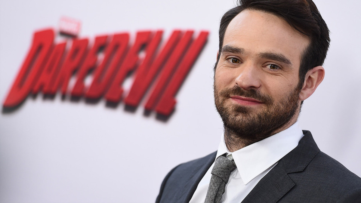 Charlie Cox poses in front of a Daredevil sign.
