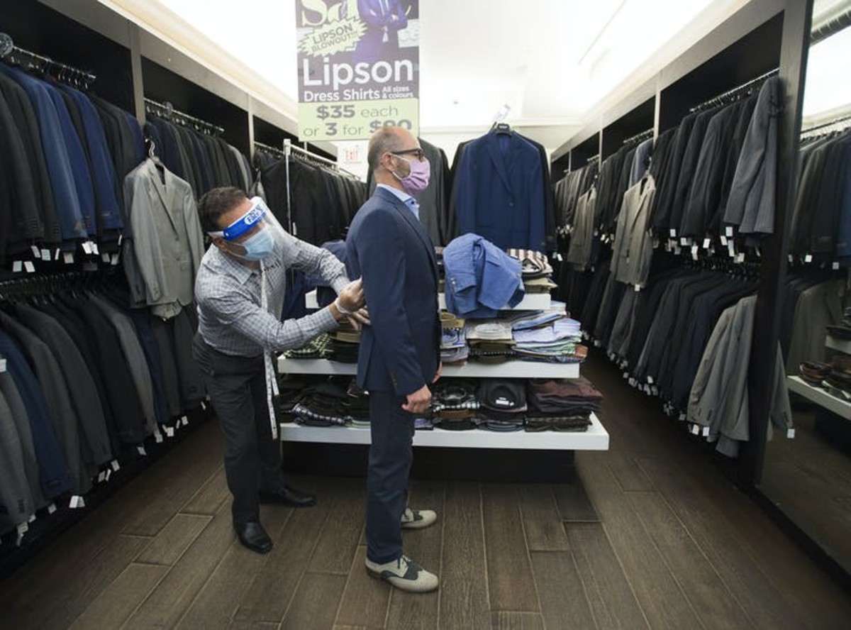 Head tailor Soheil Khorrami, left, demonstrates a safe way to fit a blazer for a customer at Tom’s Place in Kensington Market in Toronto in June 2020. THE CANADIAN PRESS/Nathan Denette