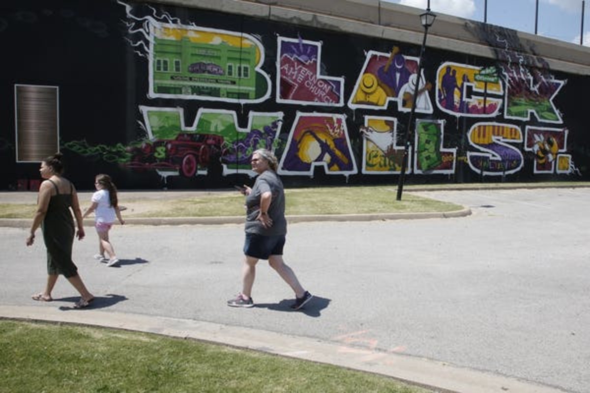 In this June 15, 2020, photo, people walk past a Black Wall Street mural in the Greenwood district in Tulsa, Okla. Dozens of blocks of Black-owned businesses were destroyed by a white mob in deadly race riots nearly a century ago. (AP Photo/Sue Ogrocki)