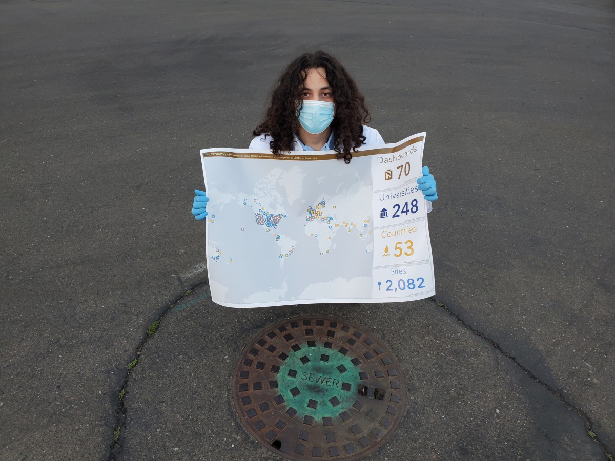 Fernando Adali Roman, Jr., a recent graduate from the Environmental Engineering program at UC Merced, is pictured over a manhole with a printout of the COVIDPoops19 dashboard.