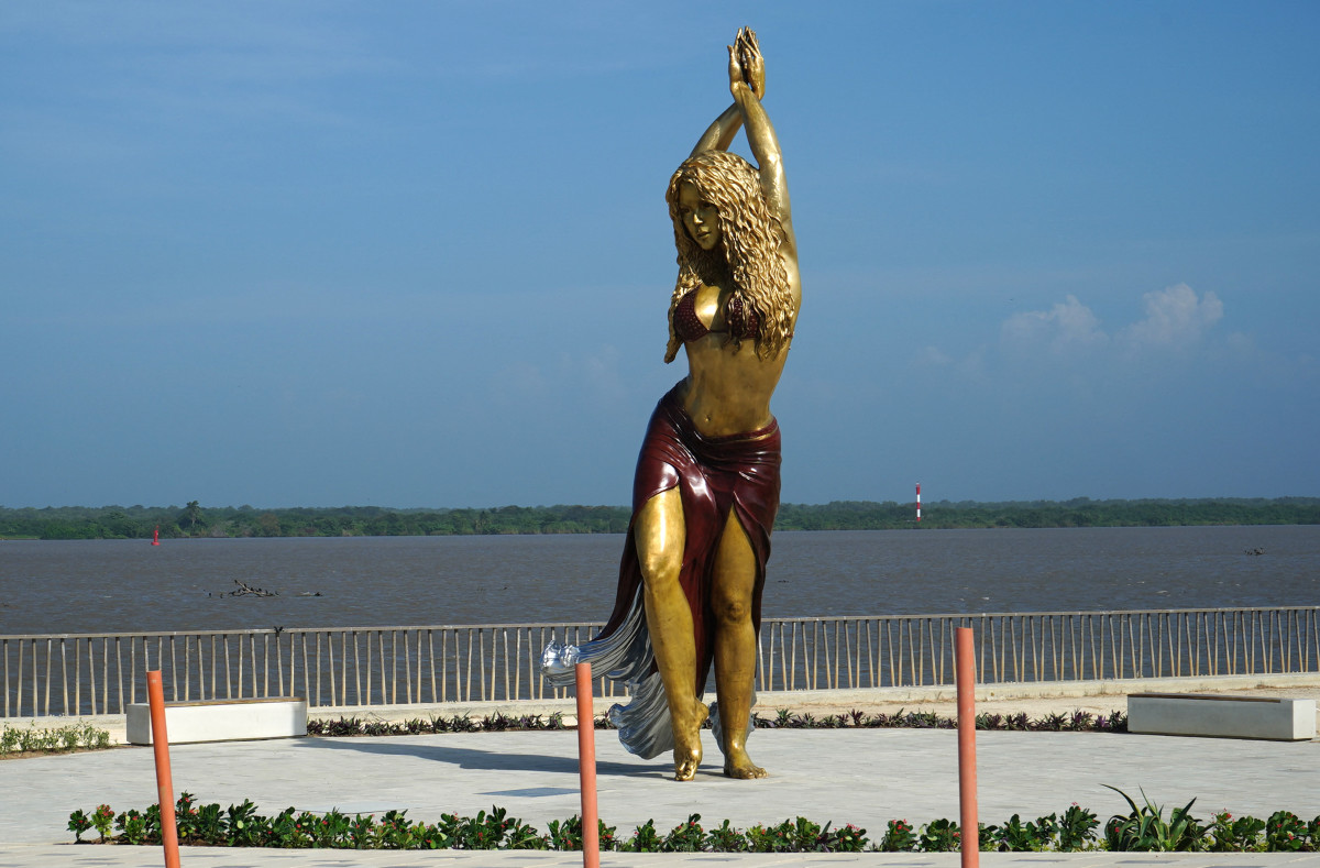 Photograph of bronze Shakira statue on the Barranquilla waterfront with a blue sky and the sea in the background