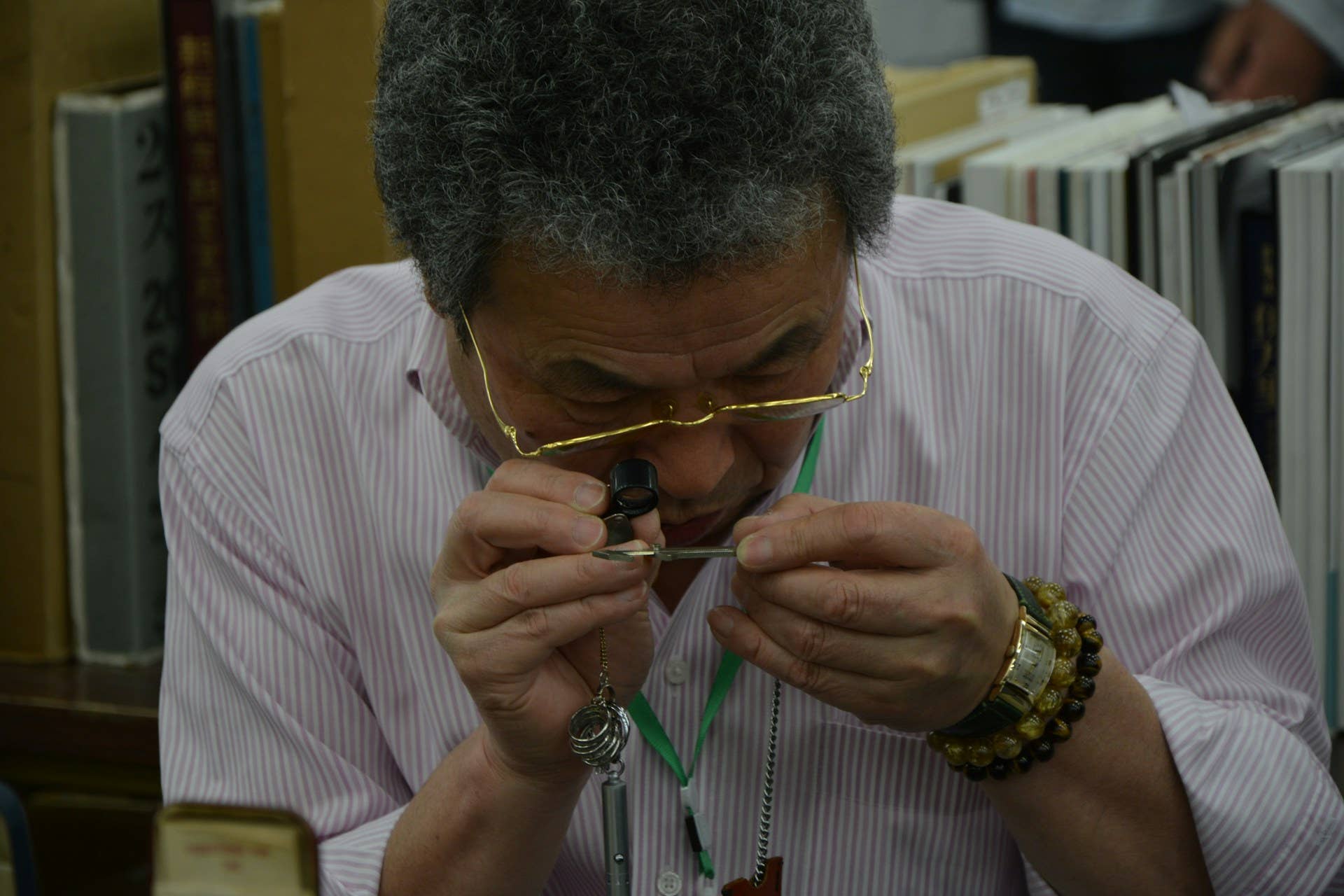 年配の男性が書店や書庫で宝石商のルーペを使って小さなアイテムを調べています。
